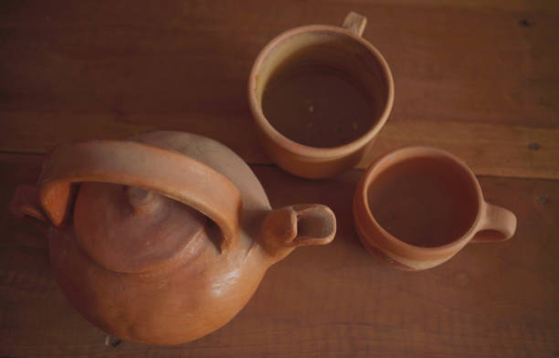 Earthenware kettle and mugs on wooden table background.