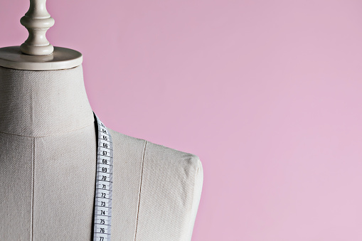 Tailor Mannequin with measure tape in front of pink background.