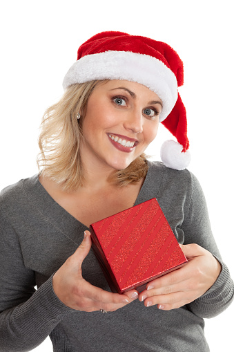 Middle aged joyful woman holding a red Christmas gift box wearing a Santa hat isolated on a white background