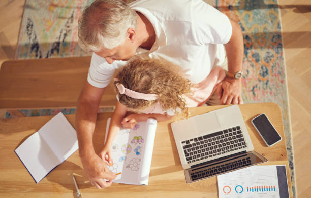istock Top view, old man and girl learning drawing while her grandfather is busy with paperwork in family home office. Senior grandfather helping and teaching a creative child to color in a school project 1445773312