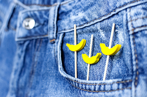 Blue jeans and yellow wooden bananas from a pocket on black background top view flat lay. Detail of nice blue jeans. Jeans texture or denim background. Trend clothing. Fashion, Selective focus.