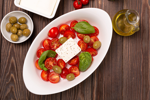 Cherry tomatoes with salted cheese, basil and olives in a deep dish prepared for baking, open space