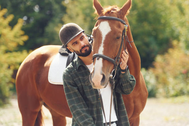 istock In protective hat. Young man with a horse is outdoors 1445775441