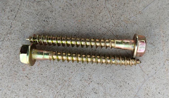Gold colored screws. Close-up on screws, metal screws, iron screws, concrete screws on surface. Concrete masonry screw with hex flange head pentagon. Screw for concrete wall using with drilling machine.