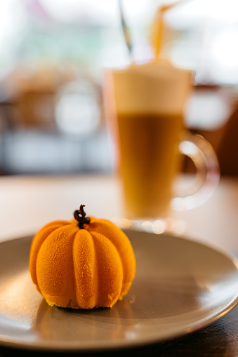 Close-up of a pumpkin-shaped mini cake with coffee on the table in a café.