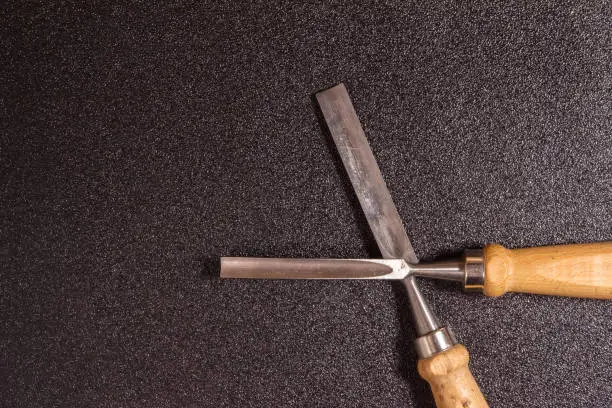 two crossed wooden-handle chisel on a black speckled background top view