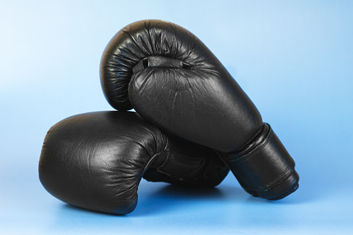 Pair of black leather boxing gloves on a blue background. Amateur boxer equipment, sports equipment.