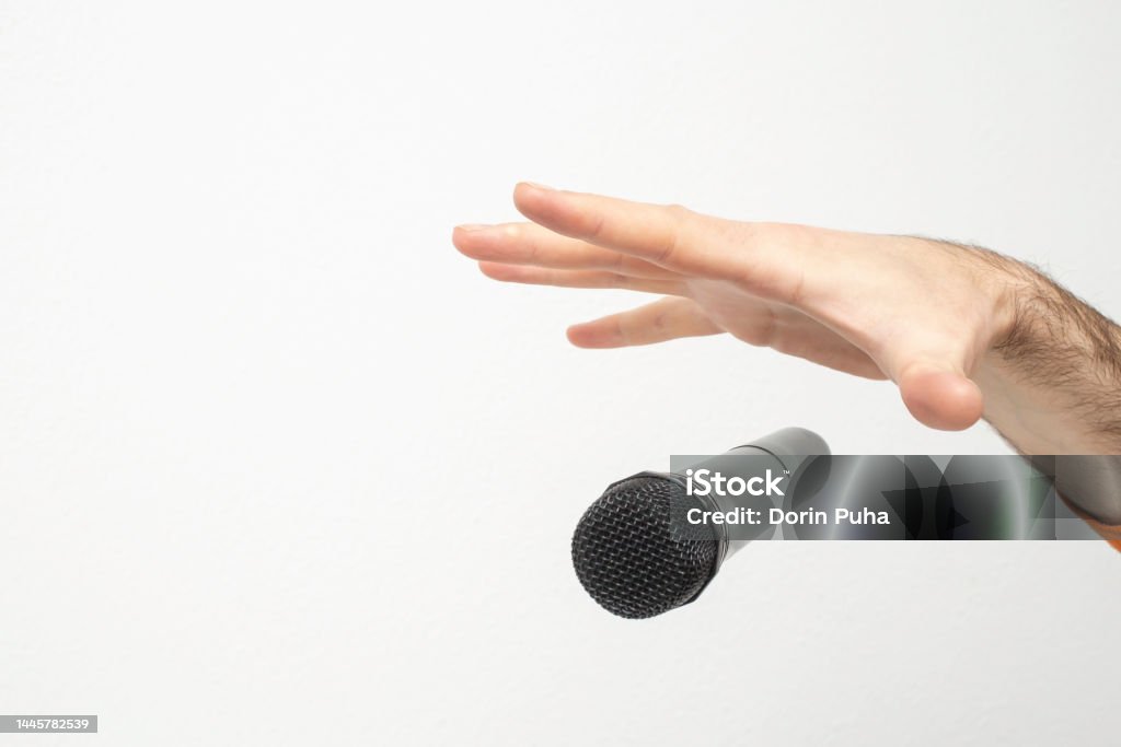 Caucasian male's hand dropping the mic, stretched hand and a microphone Caucasian male's hand dropping the mic, stretched hand and a microphone soft focus close up isolated on white background Microphone Stock Photo
