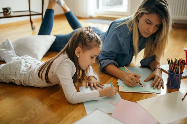 Woman spending some great time with little girl at home and they are drawing together Young woman and little girl are playing and and drawing and coloring together in their living room while lying on floor. Woman is girl's aunt and nanny. They are beautiful and playful nanny stock pictures, royalty-free photos & images