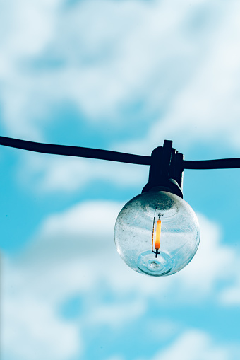 small hanging light bulb under the blue sky and white clouds with cyan color style.