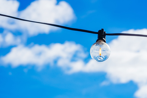 small hanging light bulb under the blue sky and white clouds