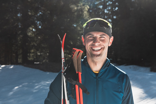 Portrait handsome male athlete with cross country skis in hands and goggles, training in snowy forest. Healthy winter lifestyle concept. High quality photo