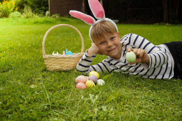 istock A boy with hare ears lies on the grass with colorful eggs. Egg hunting is an Easter tradition. 1445795966