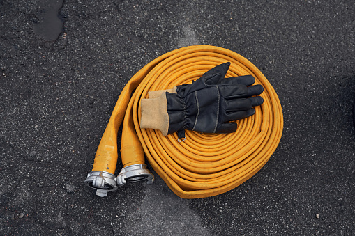 Top view of yellow fire hose with black gloves on it on the ground.