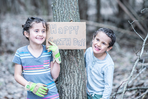 A sweet brother and sister duo hold up a sign against a tree that reads 
