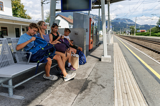 Mother and teenage kids waiting for the train on the Austrian train station. \nCanon R5