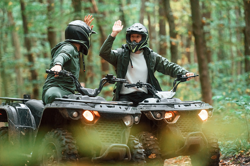 Giving high fives by the hands. Two male atv riders is in the forest together.