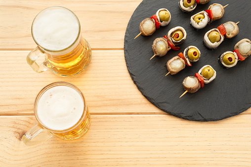 Traditional spanish tapa and two beer mugs on a wooden table.