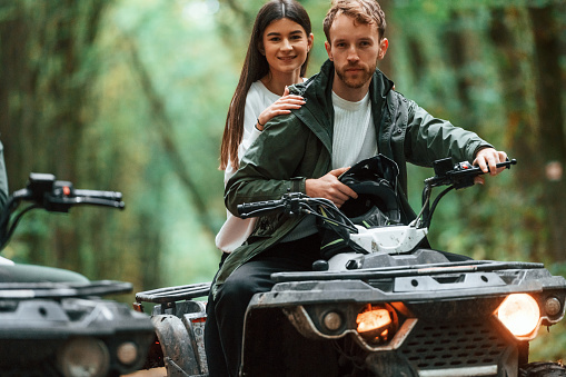 Man is handling the transport. Young couple riding a quad bike in the forest.