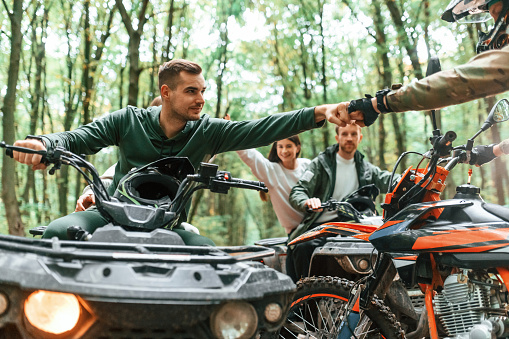 Knocking fists, gesture. Two couples on ATV with man that is on the bike in the forest.