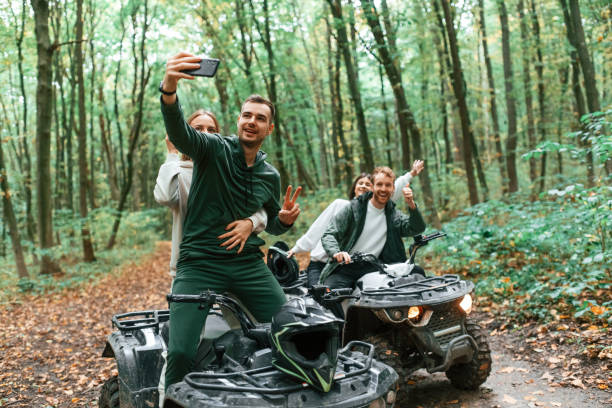Making a selfie by smartphone. Two couples on a quad bike in the forest during the day Making a selfie by smartphone. Two couples on a quad bike in the forest during the day. motorcycle 4 wheels stock pictures, royalty-free photos & images