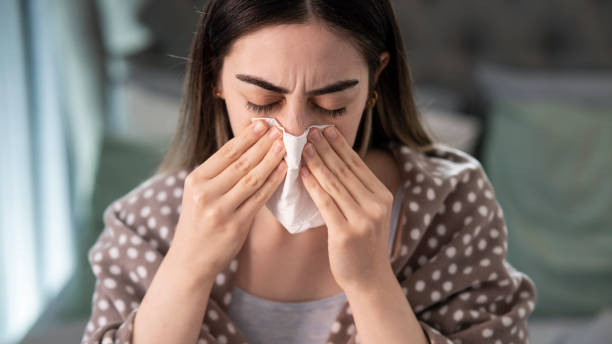 istock Young sick woman blowing her nose while in bed 1445802514