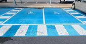 Double free parking space reserved for the disabled on blue asphalt with the international handicap symbol painted in white with the bright blue of the parking space with vehicles next to it. The space is clearly marked on both sides with additional white