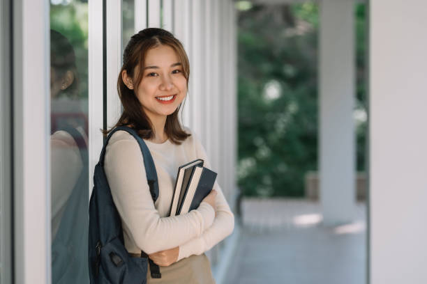 Cute Asian female student standing holding a book looking at the camera. stock photo