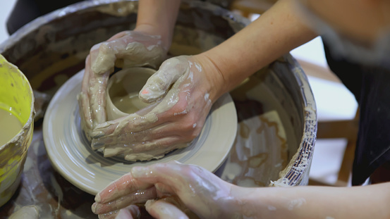 The hands of a child on a potter's wheel sculpt a pot. ART. The hands of an adult and a child in close-up are engaged in pottery at the festival.