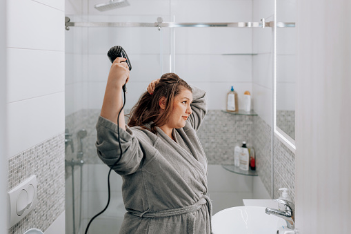 Beautiful young Caucasian plus size woman making a hairstyle after shower