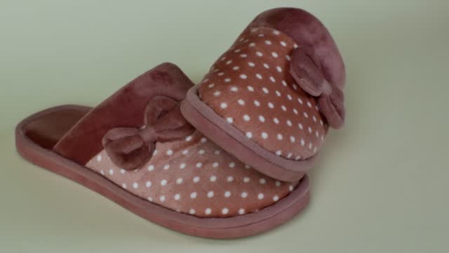 Pair of new women's slippers with beautiful pink pattern with white polka dots and a bow. Warm and comfortable female slippers on light background close-up. Concept of cozy and comfortable home shoes