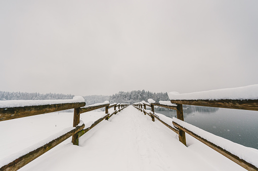 Frozen footpath with a wooden fence by the lake on a snowy winter morning.
