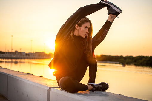 Young fit woman practicing yoga with one leg raised wearing sportswear outdoors at sunset