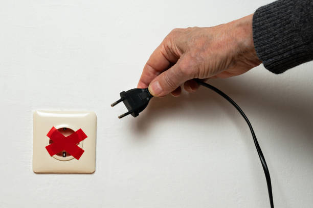 la mano di un uomo sta cercando di collegare una spina a una presa elettrica sigillata con nastro isolante rosso. crisi energetica globale. - electric plug outlet human hand electricity foto e immagini stock