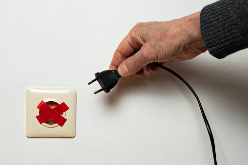 A man's hand is trying to plug a plug into an electrical outlet that is sealed with red electrical tape. Global energy crisis. Close-up.