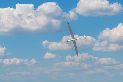 A light glider plane flies in the blue sky with white clouds.