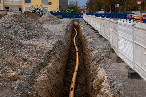 Trench with orange plastic pipe laid in it at construction site. Trench with orange plastic pipe laid in it at construction site. Fencing made of white and blue plastic barriers. trench stock pictures, royalty-free photos & images