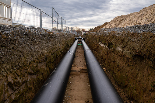 Two large metal pipes with a plastic sheath laid in a trench. Modern pipeline for supplying hot water and heating to a residential area