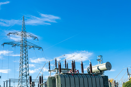 An electrical transformer and a high-voltage mast against a blue sky with light clouds.