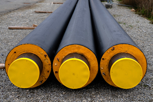 Three isolated heating pipes with yellow plastic plugs lie on a construction site. Close-up.