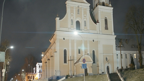 Old Catholic Church in night city. Action. Beautiful light temple illuminated at night. Catholic church with tower in modern city.