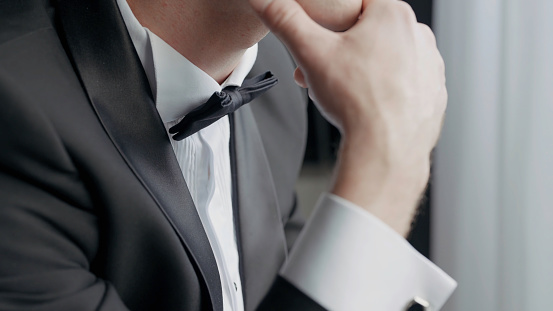 Close up of a man dressed in black and white suit with a bow tie. Action. Details of a worried male groom before the wedding ceremony