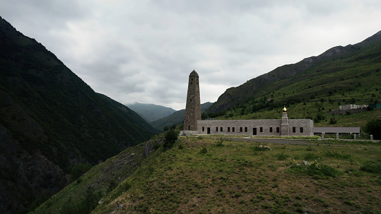 Caucasian battle tower, Ingushetia. Action. Aerial view of an ancient tower and a building on a green hill top surrounded by mountains