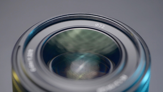 Close up of a new camera lens on blurred grey background. Action. Details of professional photographer equipment