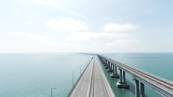 Top view of long bridge highway across sea. Action. Beautiful landscape with hinged white bridge over turquoise sea. Bridge with highway across sea on sunny day.