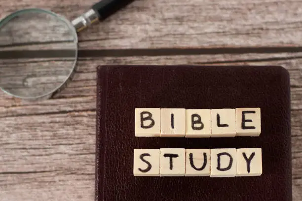 Bible study text on wood cubes, closed holy Bible Book, and magnifying glass on rustic background. Top table view. Searching, studying, and reading Christian Scriptures, biblical concept.