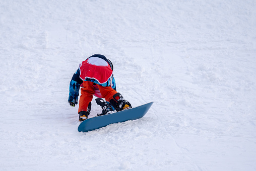 Person with snowboard on the snow. One Asian child is falling on the ground. Winter sport with copy space.