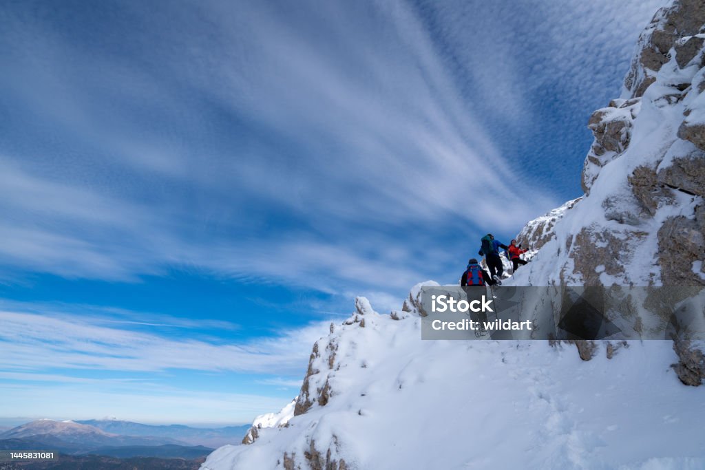 Successful mountain climber team is climbing to the summit of a mountain in winter Alpinist climbers are enjoying the climb while standing on snowy mountain crest on extreme harsh conditions. Self-discipline Stock Photo