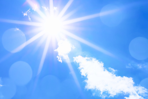 Bright sun with beautiful beams in a blue sky with some light clouds. Space for copy.