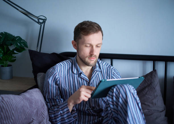 istock Man in sleepwear using tablet working, surfing or educating. Weekend concept 1445833068